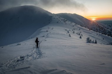 Torist silueti, yüksek kış dağlarında güzel günbatımını seyrediyor.