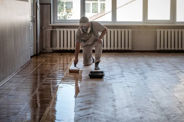 漆塗りの寄木細工床 プロの労働者は床をコーティングするためにローラーを使用する — ストック写真