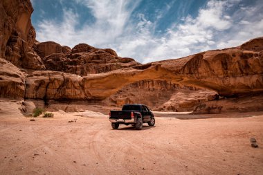 Wadi Rum çölündeki bir kaya kemerinden görünen off-road arabası. Ürdün