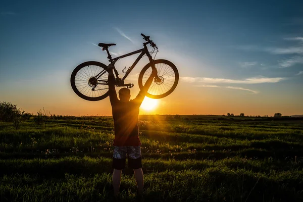 Silhouette Mannen Stå Åtgärd Lyft Cykel Ovanför Hans Huvud Ängen — Stockfoto