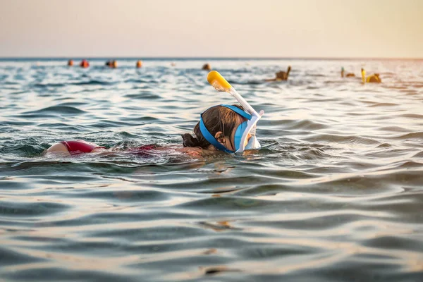 Woman in full face snorkeling mask swims in the sea at sunset