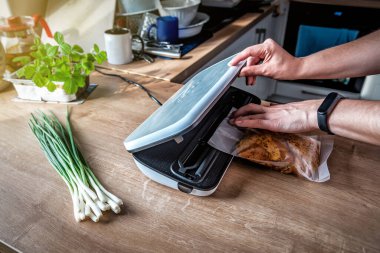 Woman using vacuum seal machine for vacuum packing meat in plastic bags. Bunch of green onion on the table
