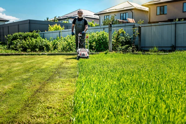 Man mowing lawn in the backyard of his house. Man with lawn mower under sunlight