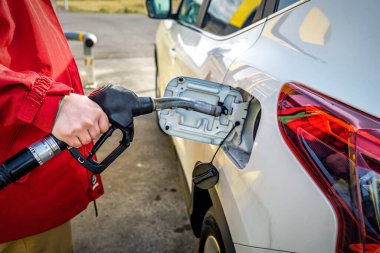 Beyaz bir arabaya yakıt ikmali yapan bir erkek. Daha yüksek petrol fiyatları. Ulaşım teması
