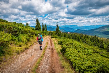 Sırt çantalı turist bulutlu gökyüzünün altındaki dağlarda yürüyor