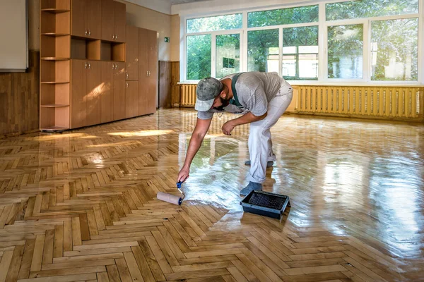 漆塗りの寄木細工床 労働者は床をコーティングするためにローラーを使用する 塗装ローラーで漆塗りの寄木細工の床をニス 2層目 住宅改修の寄木細工 — ストック写真