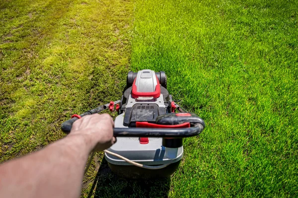 Man hand holding a lawn mower machine to cutting green grass. Gardening concept. Point of view