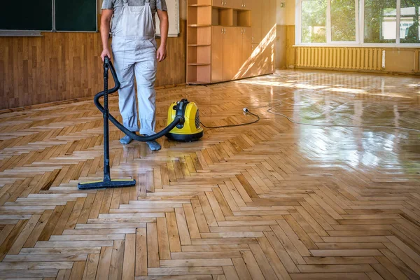 Worker cleans the parquet floor with professional vacuum cleaner. Industrial theme