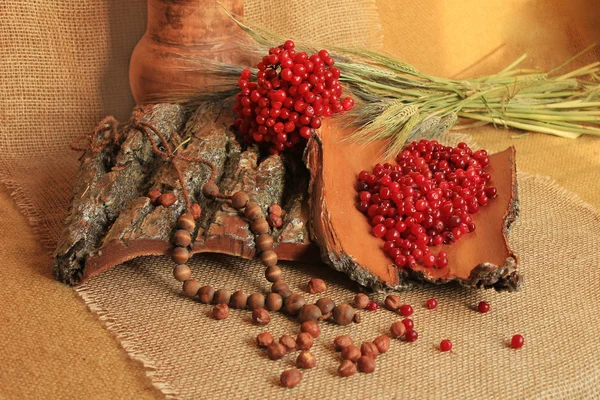 Jar of clay with bark and berries, along with nuts, wheat on linen tablecloth — Stock Photo, Image