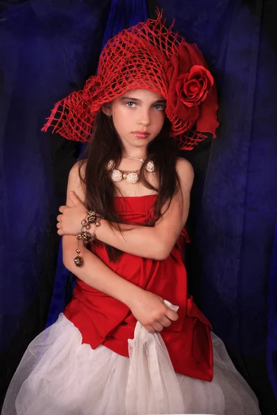 Menina em um chapéu vermelho com uma rosa em um fundo escuro Fotografia De Stock