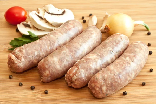 Uncooked sausages with vegetables on the chopping board — Stock Photo, Image