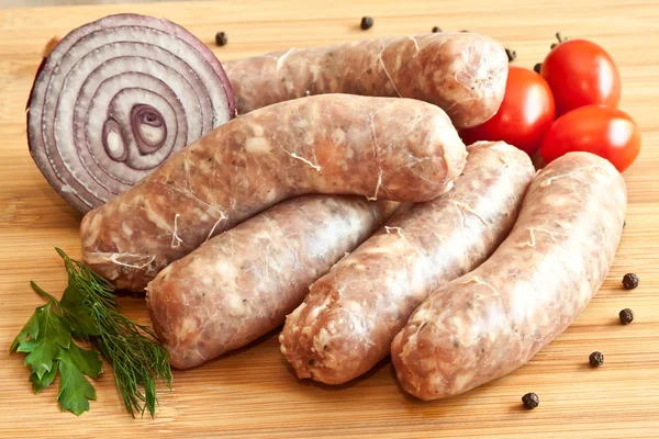 Uncooked sausages with vegetables on the chopping board — Stock Photo, Image