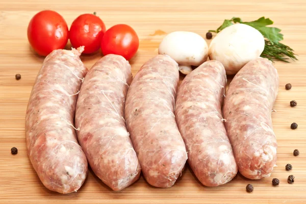 Uncooked sausage with vegetables on the chopping board — Stock Photo, Image