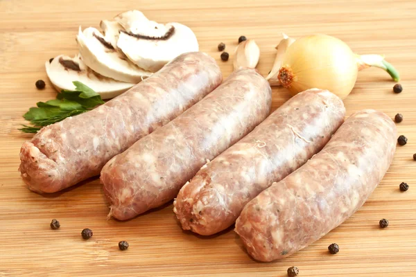 Uncooked sausages with vegetables on the chopping board — Stock Photo, Image