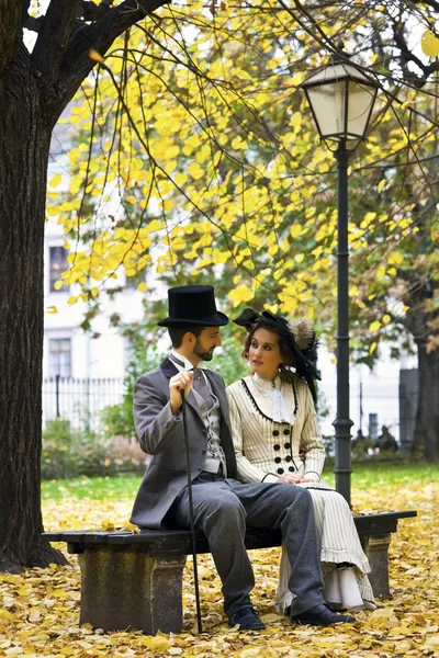 Casal vestido à moda antiga em um banco de parque no outono . — Fotografia de Stock