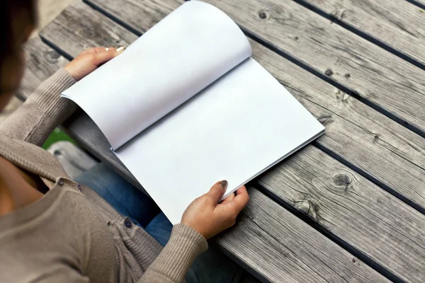 Ung kvinna sitter vid bordet med ett häfte med vita sidor — Stockfoto