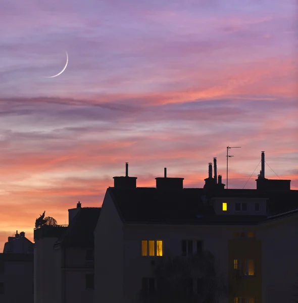 Sunset over urban rooftops with lights from some home windows. — Stock Photo, Image