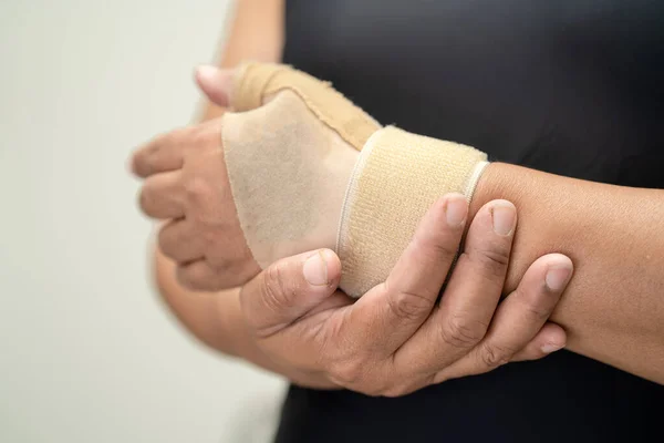 Asian middle-aged lady woman use elastic bandage to treating De Quervain syndrome at hand and finger in office.