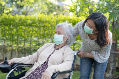 Elektrikli sandalyedeki yaşlı kadın ve yaşlı kadına yardım edin ve parktaki Covid-19 Coronavirus 'un güvenlik enfeksiyonunu korumak için maske takın..