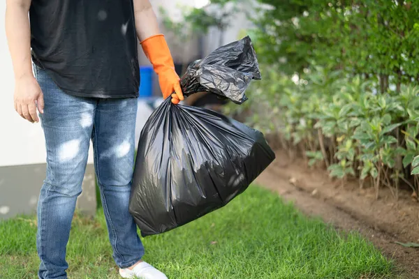 Kaldırımda siyah plastik çöp torbaları taşıyan bir kadın. Temiz çevre kavramı..