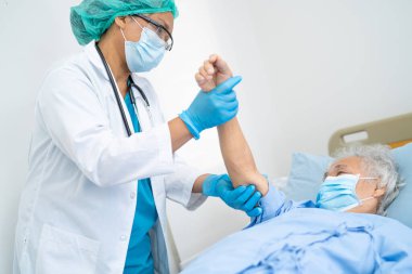 Doktor, güvenlik enfeksiyonunu korumak ve Covid-19 Coronavirus 'u öldürmek için hastanede maske takan yaşlı ve yaşlı bir kadına yardım ediyor..