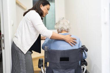 Bakıcı, Asyalı ya da yaşlı bir kadına yardım ediyor tekerlekli sandalyede oturan yaşlı kadının evde merdivenlerden çıkmasına yardım ediyor..