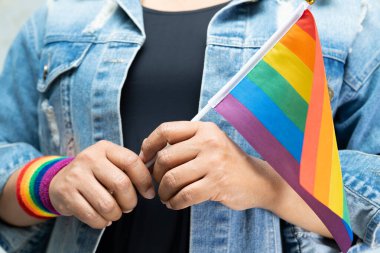 Mavi kot ceket ya da kot pantolon giyen ve elinde gökkuşağı renkli bayrak tutan Asyalı kadın, LGBT gurur ayının sembolü, Haziran sosyal ortamında eşcinsel, lezbiyen, biseksüel, transseksüel, insan hakları.