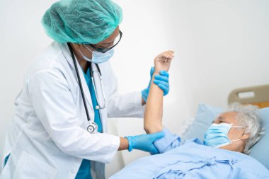 Doktor, güvenlik enfeksiyonunu korumak ve Covid-19 Coronavirus 'u öldürmek için hastanede maske takan yaşlı ve yaşlı bir kadına yardım ediyor..