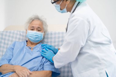 Doktor, güvenlik enfeksiyonunu korumak ve Covid-19 Coronavirus 'u öldürmek için hastanede maske takan yaşlı ve yaşlı bir kadına yardım ediyor..