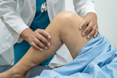Ortopedi kliniğinde kıdemli bir hastanın diz ve bacağını muayene eden Asyalı doktor fizyoterapisti..