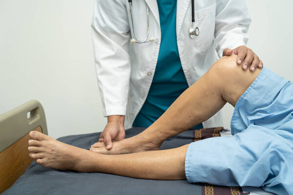 Asian doctor physiotherapist examining, massaging and treatment knee and leg of senior patient in orthopedist medical clinic nurse hospital.