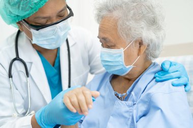 Doktor, güvenlik enfeksiyonunu korumak ve Covid-19 Coronavirus 'u öldürmek için hastanede maske takan yaşlı ve yaşlı bir kadına yardım ediyor..