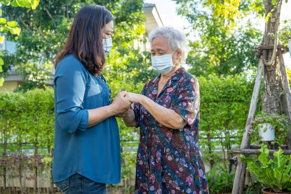 Bakıcı, doğa parkında mutlu bir şekilde yürürken Asyalı yaşlı kadına yardım ediyor..