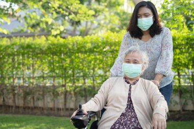 Elektrikli sandalyedeki yaşlı kadın ve yaşlı kadına yardım edin ve parktaki Covid-19 Coronavirus 'un güvenlik enfeksiyonunu korumak için maske takın..