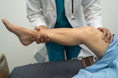 Ortopedi kliniğinde kıdemli bir hastanın diz ve bacağını muayene eden Asyalı doktor fizyoterapisti..