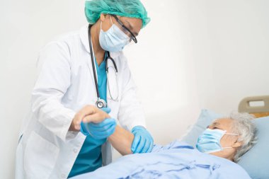 Doktor, güvenlik enfeksiyonunu korumak ve Covid-19 Coronavirus 'u öldürmek için hastanede maske takan yaşlı ve yaşlı bir kadına yardım ediyor..