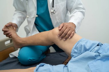 Ortopedi kliniğinde kıdemli bir hastanın diz ve bacağını muayene eden Asyalı doktor fizyoterapisti..