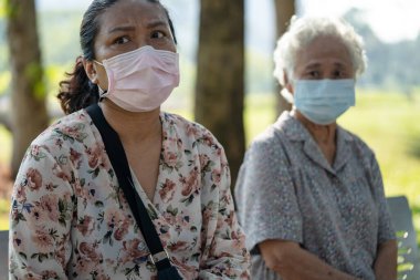 Asya 'lı yaşlı kadın ve kızı sosyal mesafelerde oturuyor ve parkta Covid 19 Coronavirus' u korumak için maske takıyor..