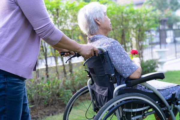 介護娘抱擁とヘルプアジアのシニアまたは高齢者の女性保持赤いバラオン車椅子で公園 — ストック写真