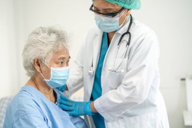 Doktor, güvenlik enfeksiyonunu korumak ve Covid-19 Coronavirus 'u öldürmek için hastanede maske takan yaşlı ve yaşlı bir kadına yardım ediyor..