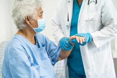 Doktor, güvenlik enfeksiyonunu korumak ve Covid-19 Coronavirus 'u öldürmek için hastanede maske takan yaşlı ve yaşlı bir kadına yardım ediyor..