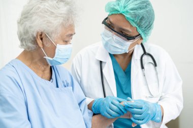 Doktor, güvenlik enfeksiyonunu korumak ve Covid 19 Coronavirus 'u öldürmek için hastanede maske takan yaşlı ve yaşlı bir kadına yardım ediyor..