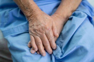 Asyalı yaşlı ya da yaşlı kadın hasta hemşire hastanesinde yatağında yatarken umutla elini tutuyor..