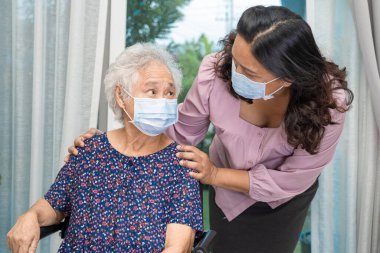 Bakıcı, Asyalı yaşlı ya da yaşlı kadın tekerlekli sandalyede oturan ve güvenlik enfeksiyonunu korumak için maske takan Covid19 Coronavirus 'a yardım ediyor..