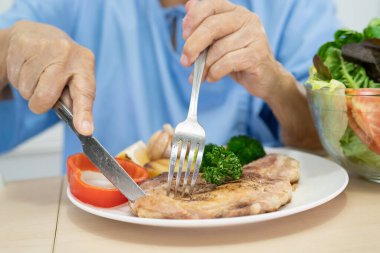 Asyalı yaşlı ya da yaşlı kadın hasta kahvaltı ve sebze yiyen umut dolu ve mutlu bir şekilde hastanede aç bir şekilde yatarken sağlıklı yiyecekler yiyor..