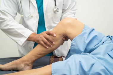 Ortopedi kliniğinde kıdemli bir hastanın diz ve bacağını muayene eden Asyalı doktor fizyoterapisti..