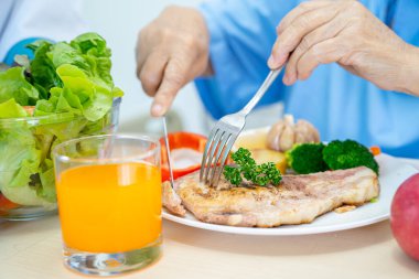 Asyalı yaşlı ya da yaşlı kadın hasta kahvaltı ve sebze yiyen umut dolu ve mutlu bir şekilde hastanede aç bir şekilde yatarken sağlıklı yiyecekler yiyor..