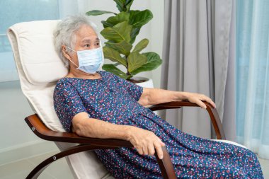 Asyalı yaşlı kadın evinde sallanan sandalyede mutlu bir şekilde oturuyor ve rahatlıyor..