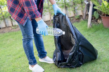 Asyalı kadın gönüllü olarak parkta çöp poşetlerine su plastik şişeleri taşıyor, çöpleri parka atıyor, çevresel ekoloji kavramını geri dönüştürüyor..