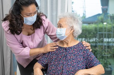Bakıcı, Asyalı yaşlı ya da yaşlı kadın tekerlekli sandalyede oturan ve güvenlik enfeksiyonunu korumak için maske takan Covid19 Coronavirus 'a yardım ediyor..